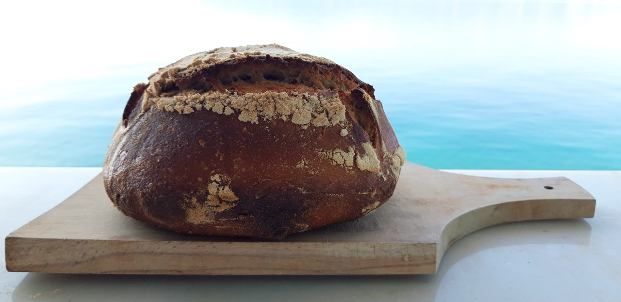 Golden sourdough boule on a board with the sea behind