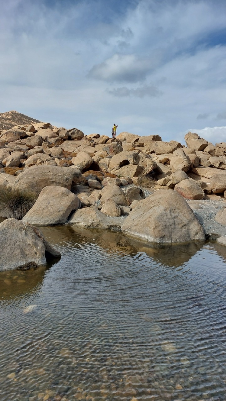 Rocky Livada shore in Tinos with a small figure standing on the boulders and still water