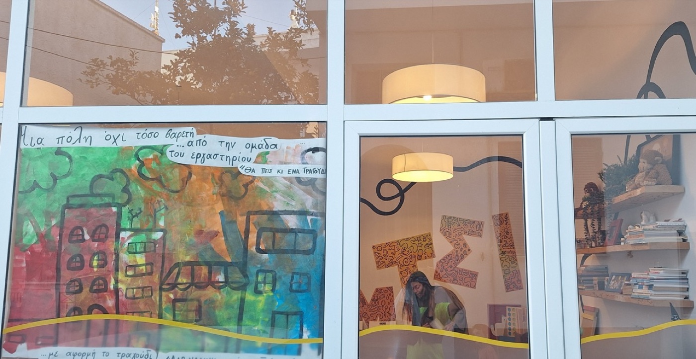 Children's painted cityscape in the window of Τούμτσι creative workshop in Tinos