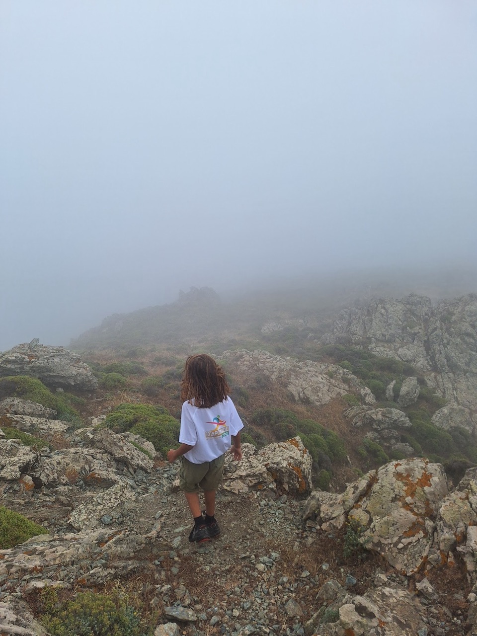 A small figure standing on a summit rock with cloud all around